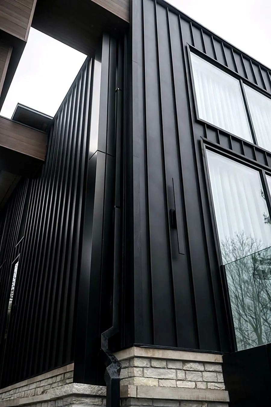 Matte black vertical metal siding beside large windows